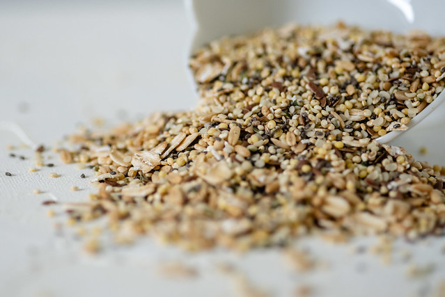 Macro de mélange premium de graines pour oiseaux se déversant d'une tasse blanche — millet doré, flocons d'avoine, lin